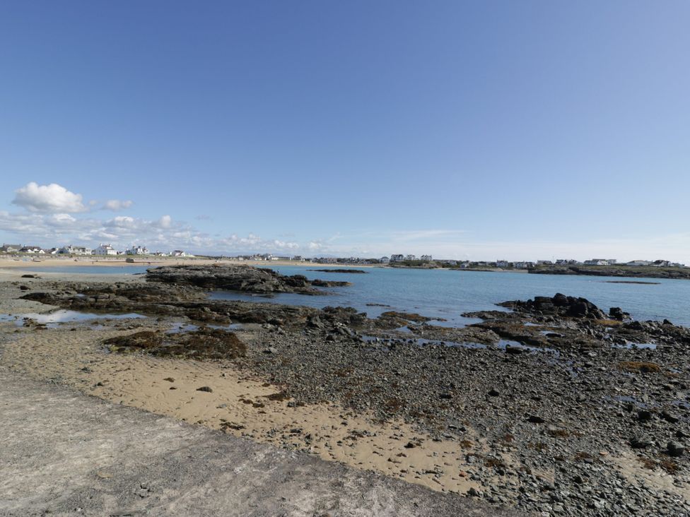 A beach view with rocks and houses in the background at Haul a Gwynt in Trearddur Bay