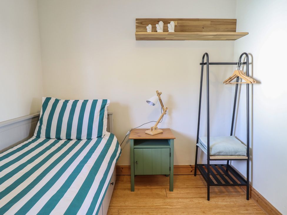 A bedroom with a bed, table, lamp, and coat rack at Redwood in Harlech