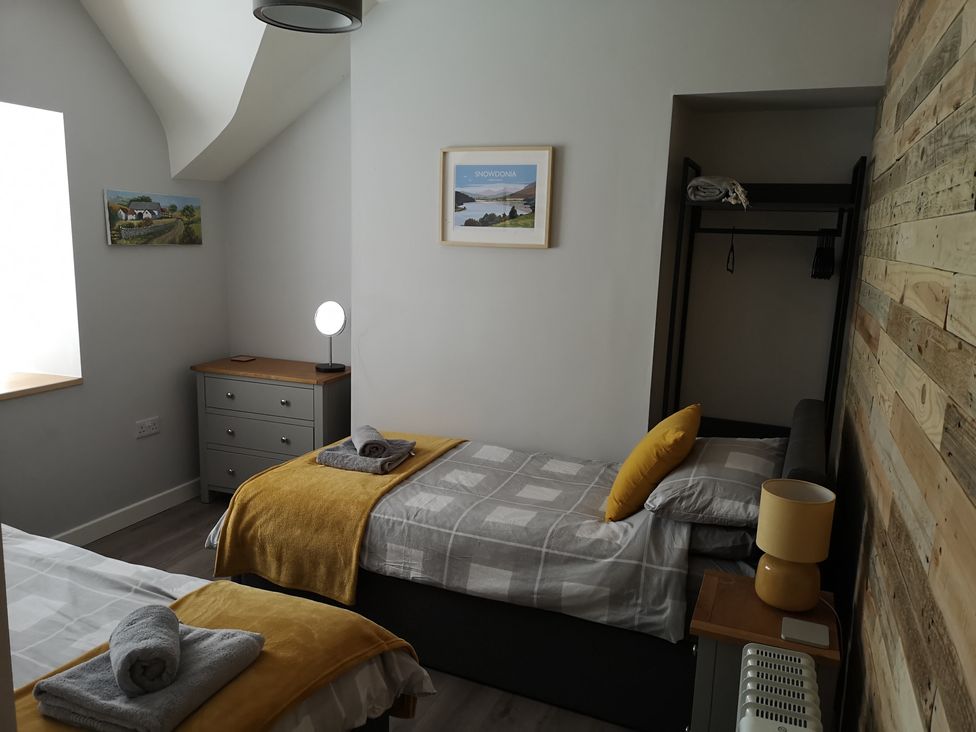 A bedroom with two single beds each with yellow blankets and gray towels on top at Y Bwthyn in Llanbedr