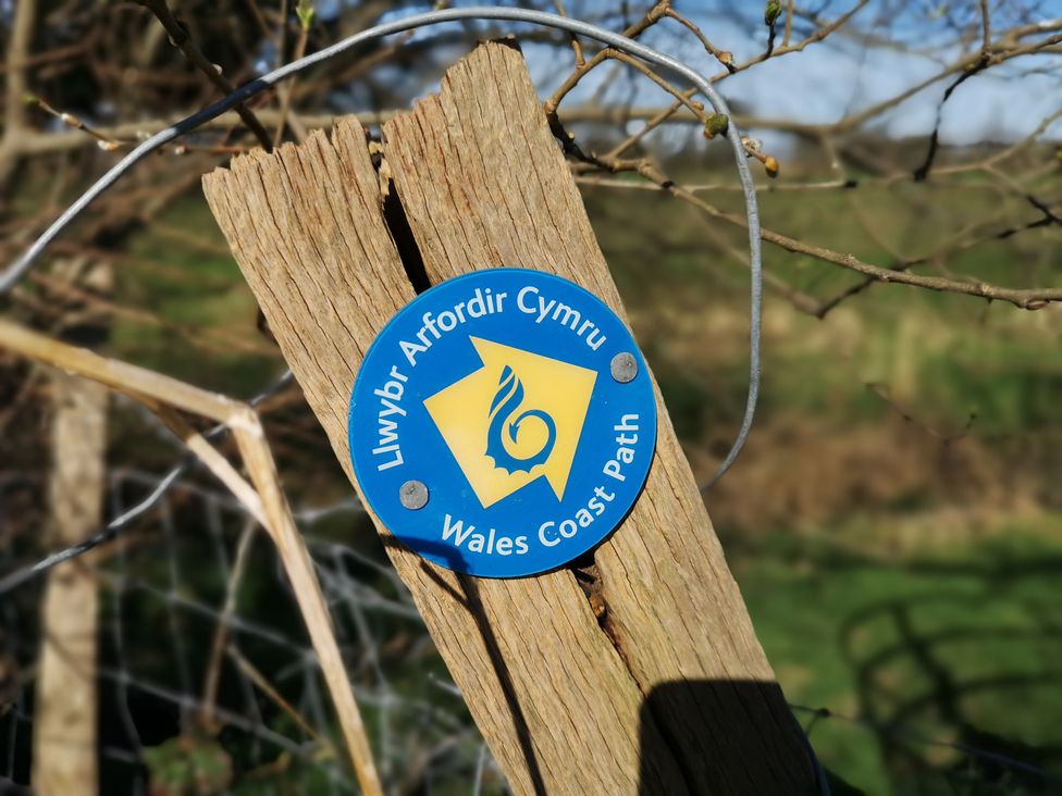 A wooden post with a circular blue and yellow Wales Coast Path sign attached outdoors at Y Bwthyn in Llanbedr