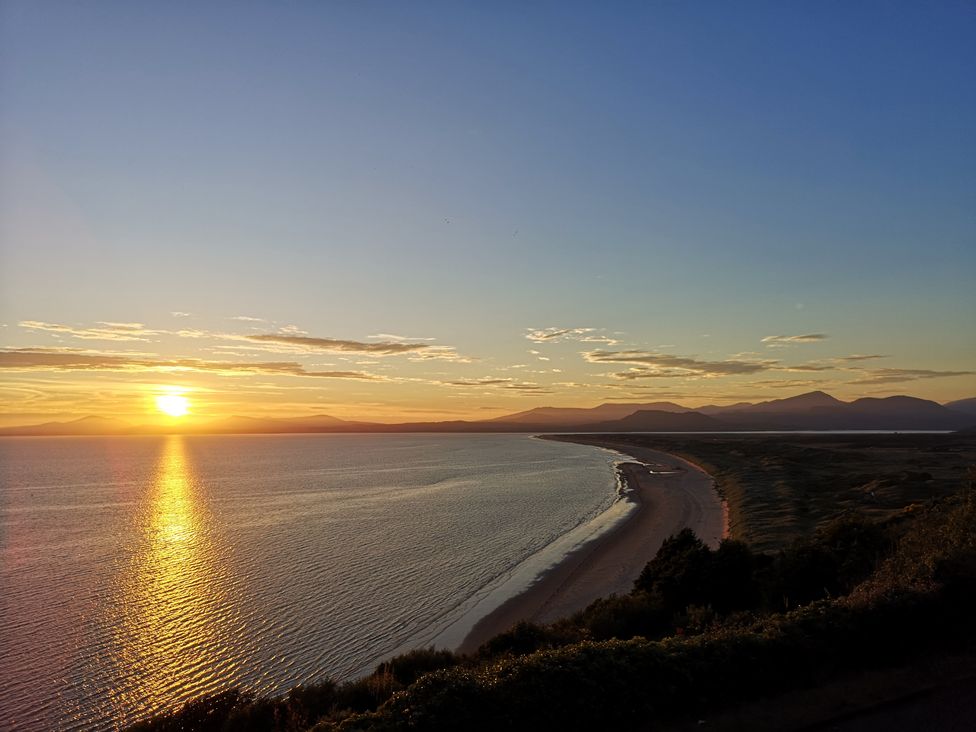 A sunset over a curved coastline with mountains in the distance at Y Bwthyn in Llanbedr