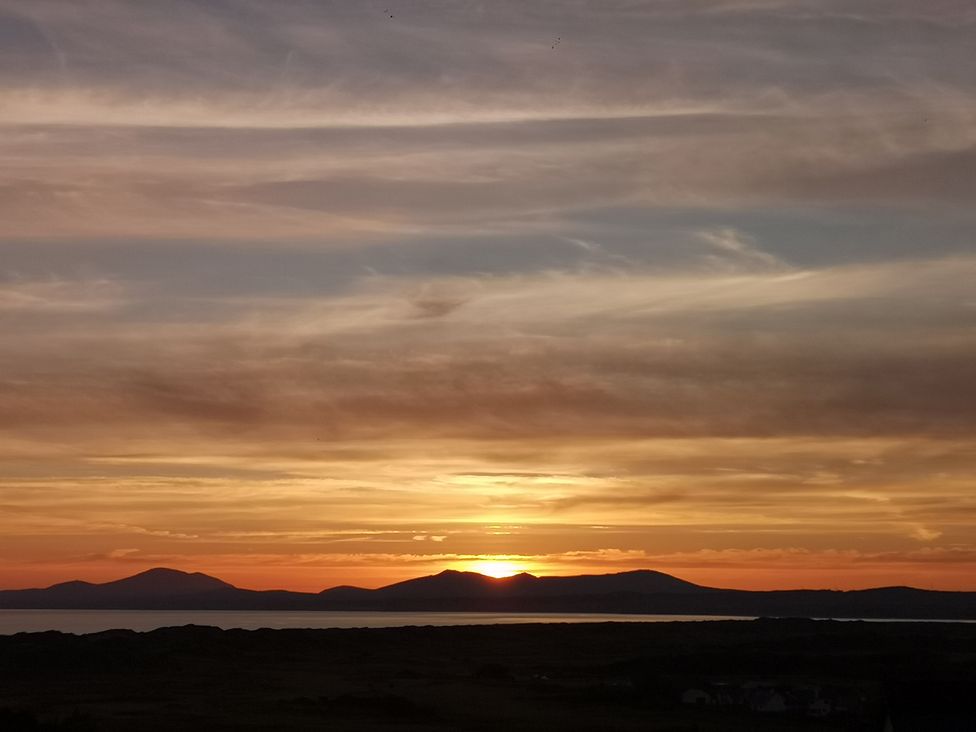 A sunset over mountains with a body of water and a dark land silhouette at Y Bwthyn in Llanbedr