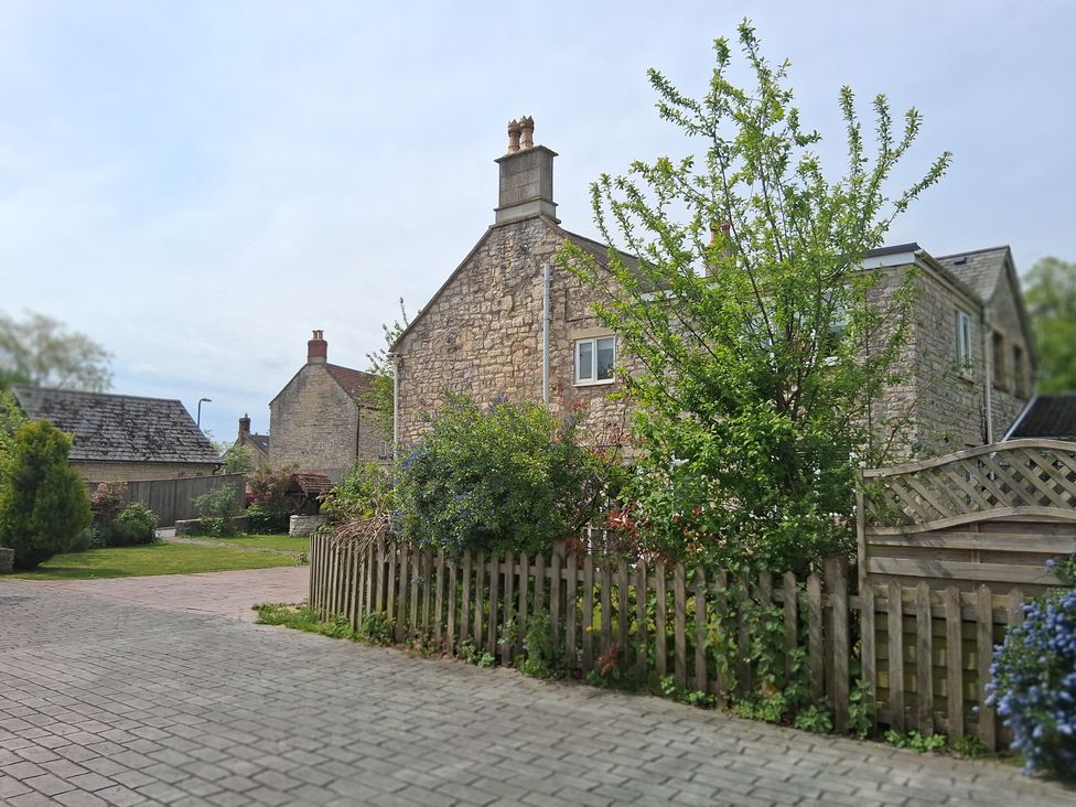 A garden with a stone house and a fence at Crooked Well in Timsbury, Nr Bath