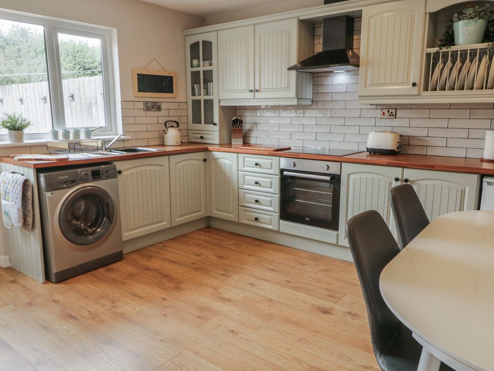 A kitchen with cabinets, washing machine, oven, and dining table at Hazel Cottage in Portrush