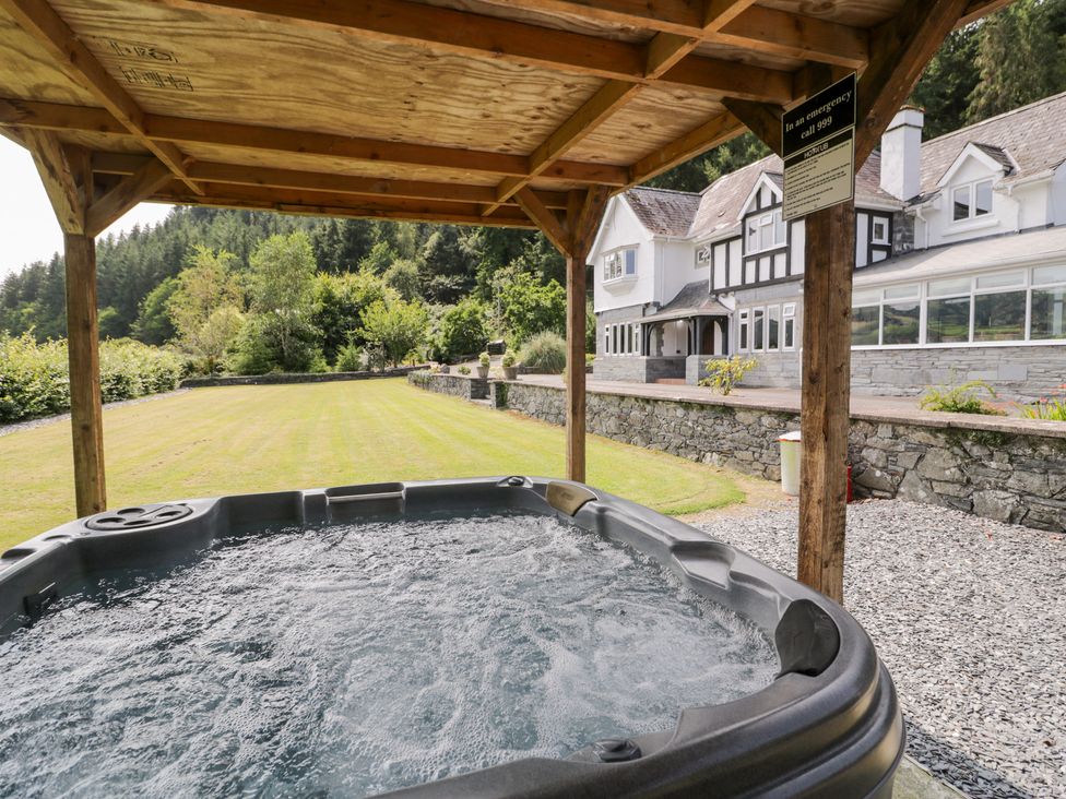 A hot tub under a wooden shelter in the garden at Pengwern in Llanrwst