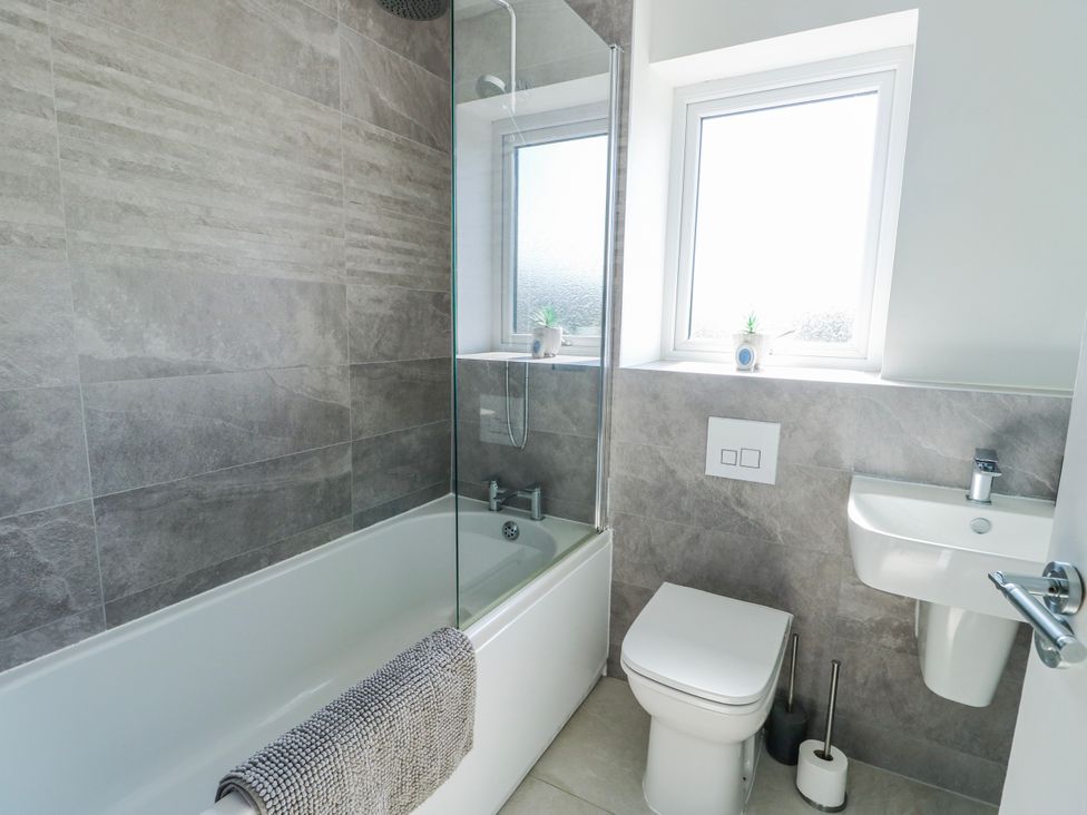 A bathroom with a bathtub, toilet, sink, and window at Dune Retreat in Llanfaelog near Rhosneigr