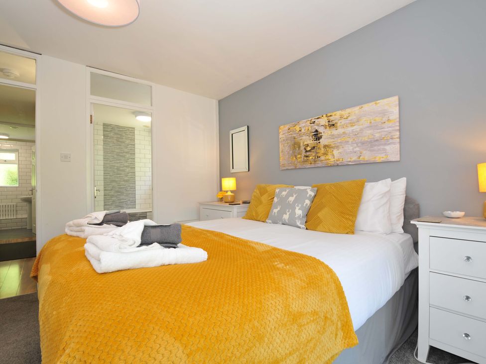 A bedroom with a double bed featuring yellow and gray cushions white bedside tables and lamps with a visible bathroom at 59 Valley Lodge Callington near Gunnislake