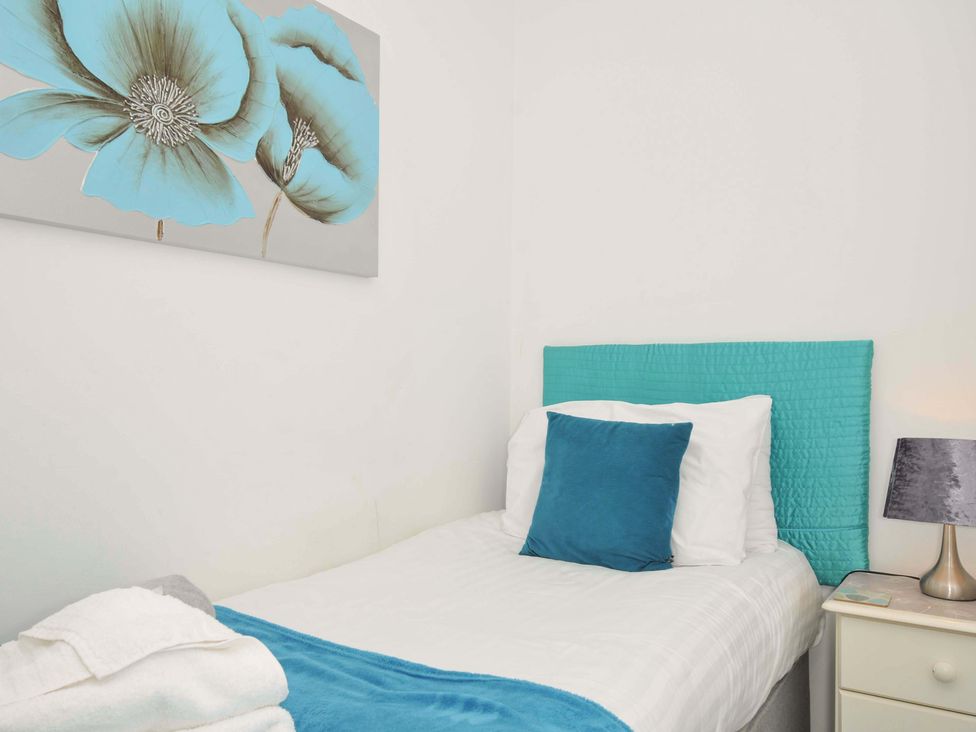A bedroom with a single bed with blue headboard and cushion next to a bedside table with a lamp at 59 Valley Lodge in Callington near Gunnislake