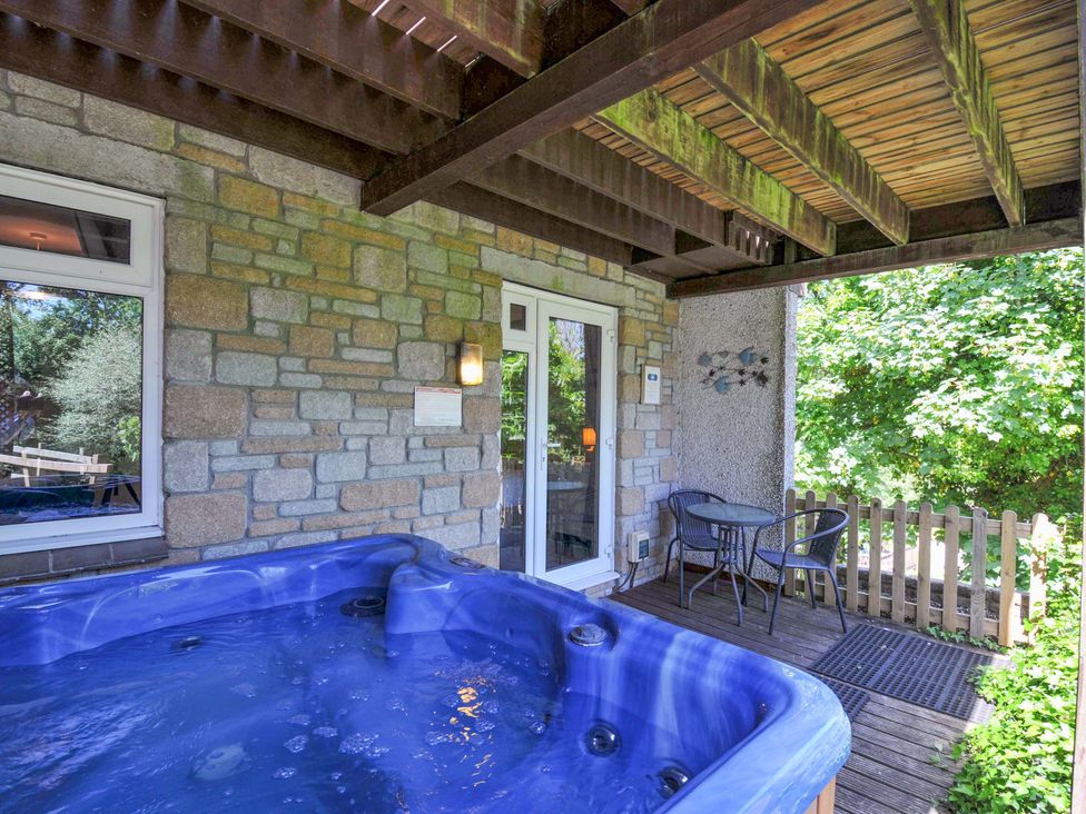 An outdoor patio with a blue hot tub a small table with two chairs wooden deck and stone wall at 59 Valley Lodge in Callington near Gunnislake
