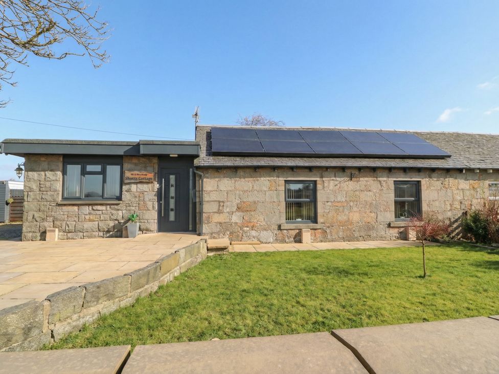 A stone building with solar panels and green lawn at Shotts Cottage Stirling