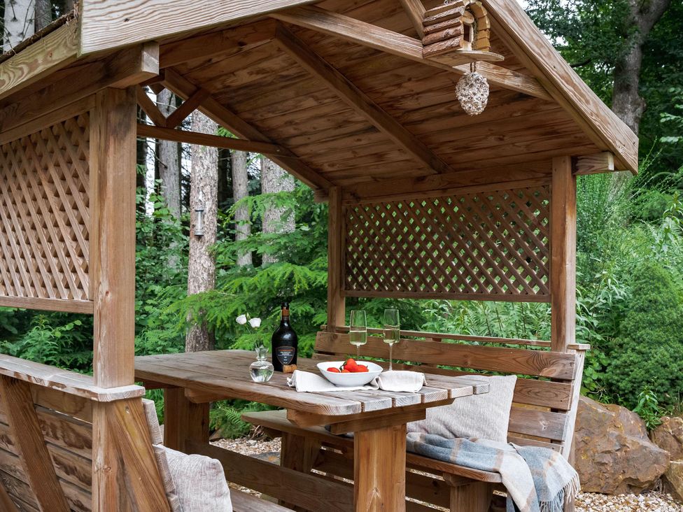 A wooden gazebo with a table set for outdoor dining at Heilan Roo in Killiecrankie near Pitlochry and Blair Atholl
