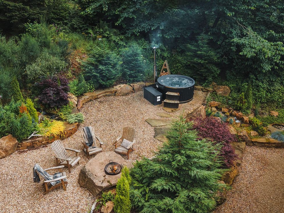 A garden with a hot tub, wooden chairs, and a fire pit at Heilan Roo, Killiecrankie near Pitlochry and Blair Atholl