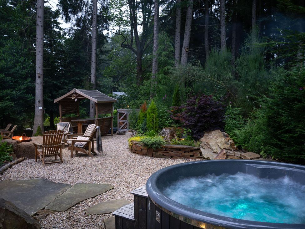 A garden with a hot tub, fire pit, wooden chairs, and a garden shed at Heilan Roo near Killiecrankie and Pitlochry and Blair Atholl