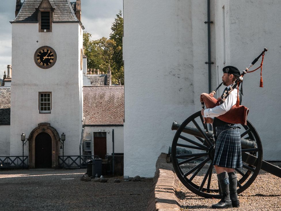A bagpiper standing near a cannon in front of a clock tower at Heilan Roo Killiecrankie near Pitlochry and Blair Atholl