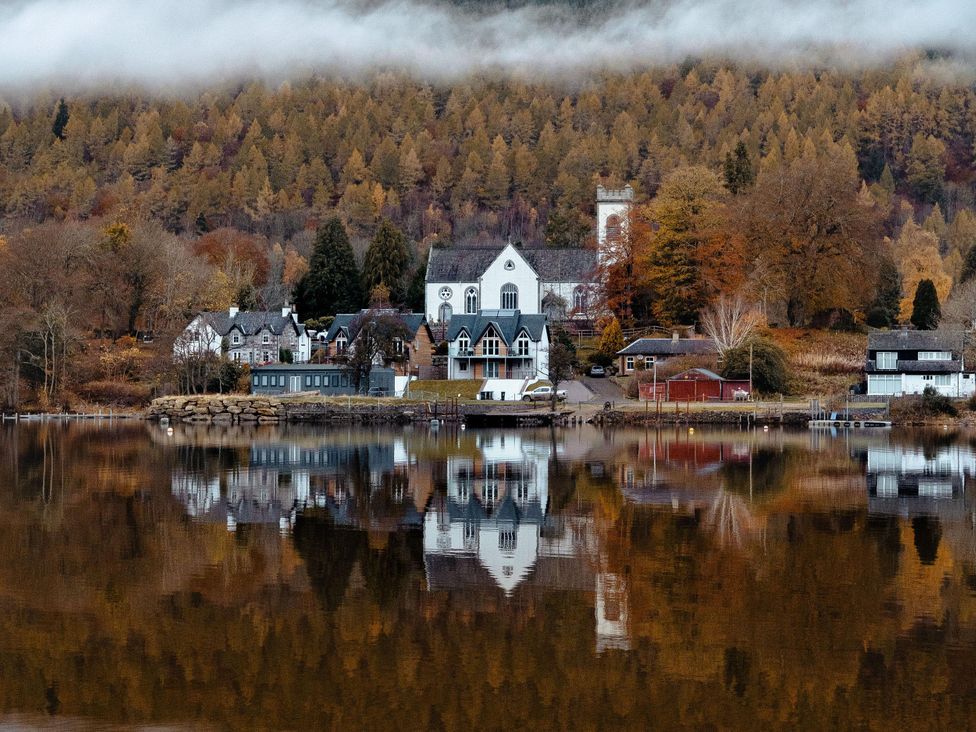 A view of houses and a church by a lake with trees in autumn at Heilan Roo Killiecrankie near Pitlochry and Blair Atholl