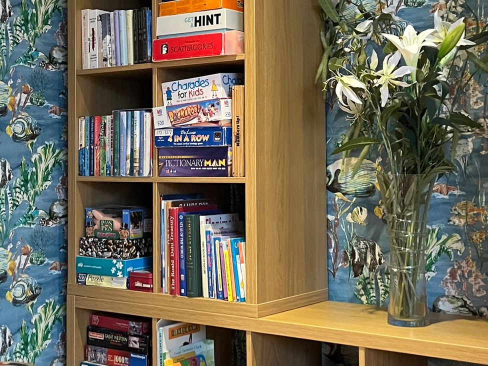 A wooden shelf with books and board games and a vase with flowers at Seasides in Weymouth