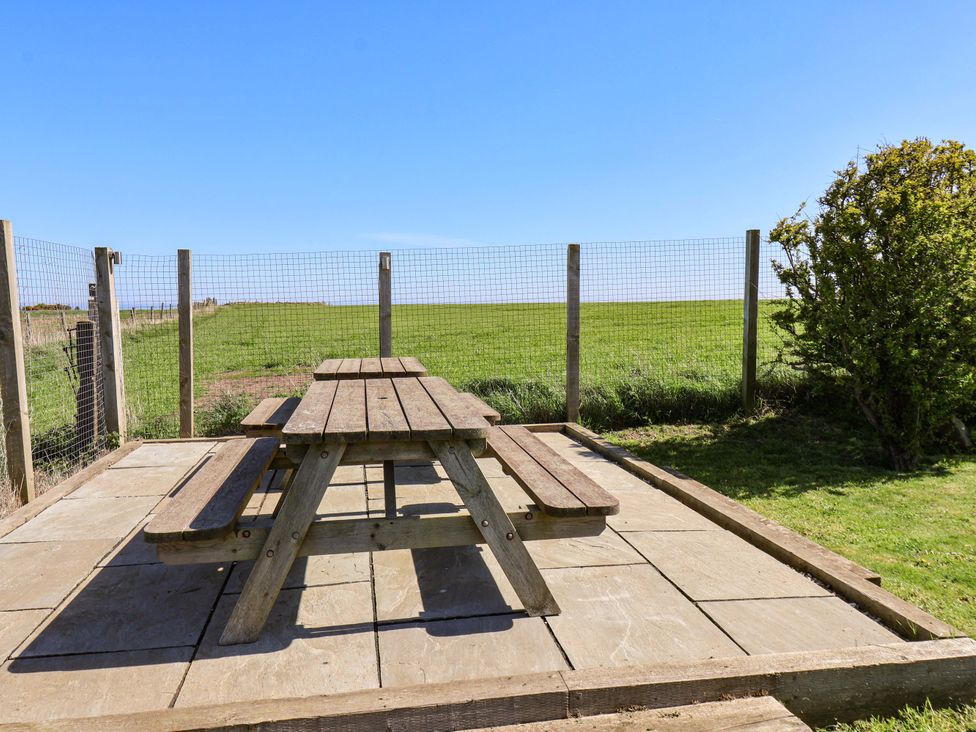 A picnic table on a patio with a grassy area at Voebroch in Lythe