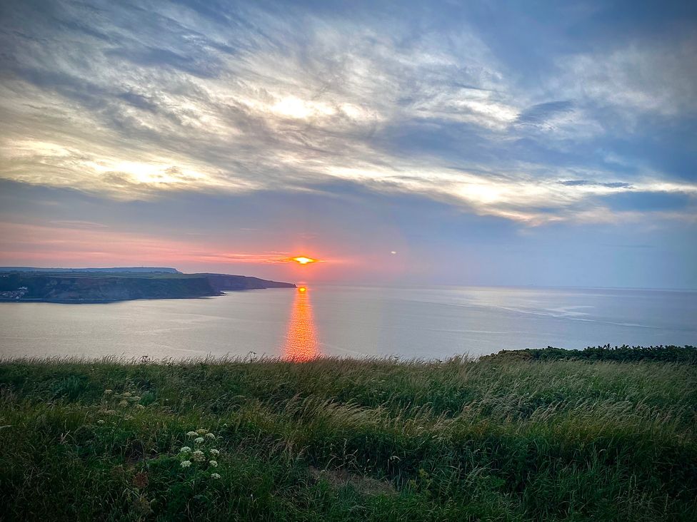 A sunset over the ocean viewed from a grassy hill at Voebroch in Lythe