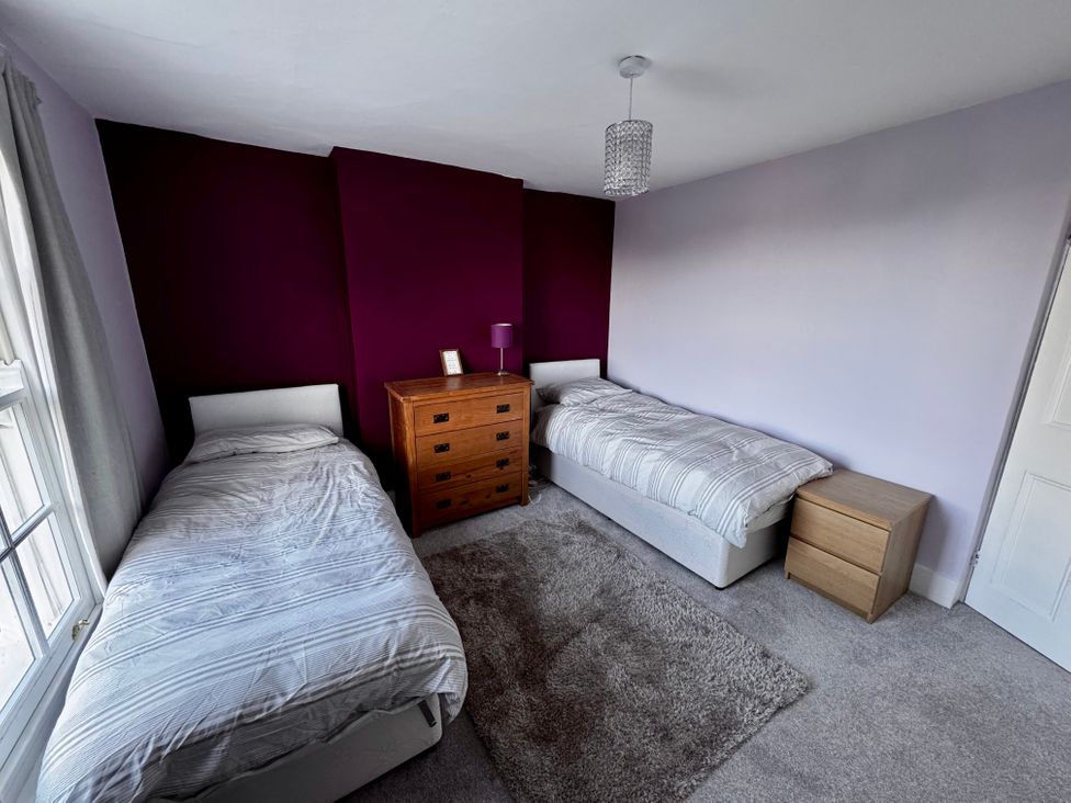 A bedroom with two single beds a wooden chest of drawers a bedside table and a rug at Overchurch in Hythe