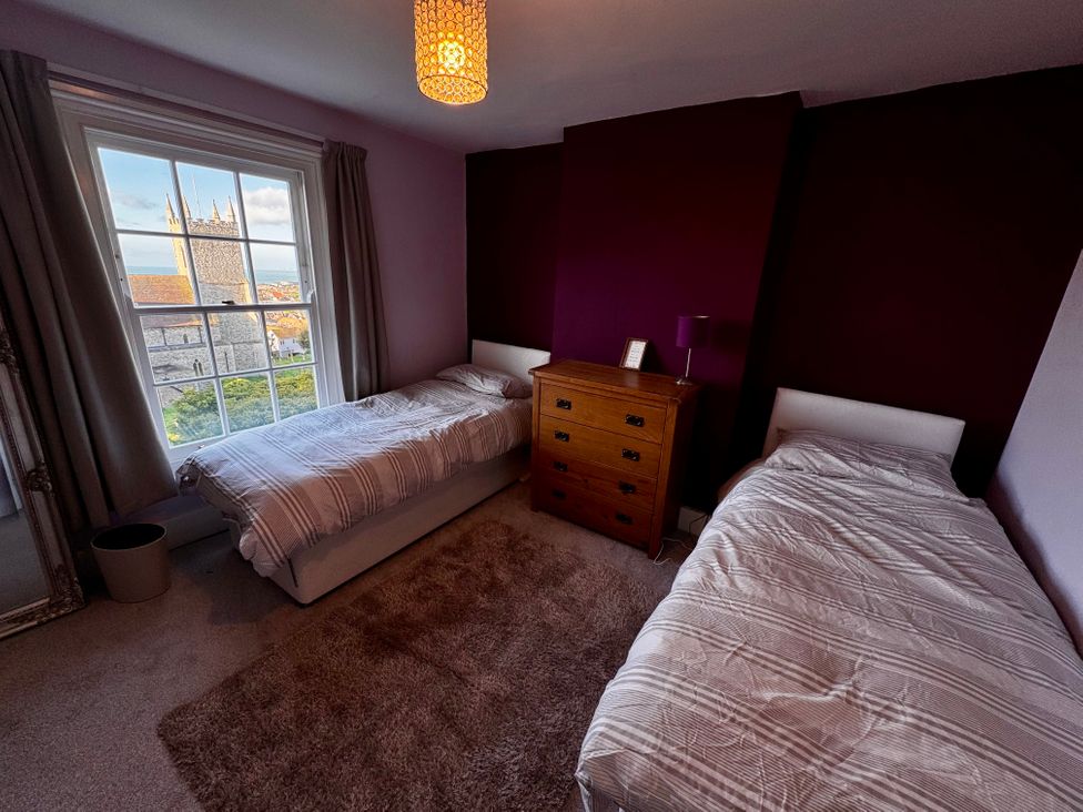 A bedroom with two single beds a wooden chest of drawers a window with curtains and a view of a church tower at Overchurch in Hythe