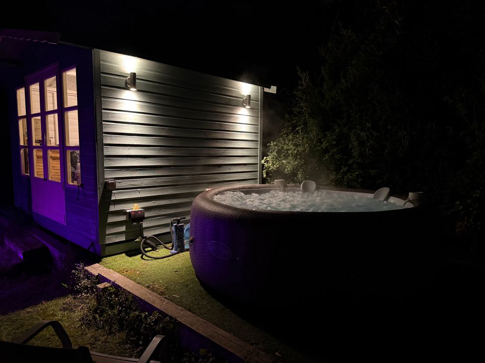 A hot tub next to a wooden building with lit outdoor lights at Overchurch in Hythe