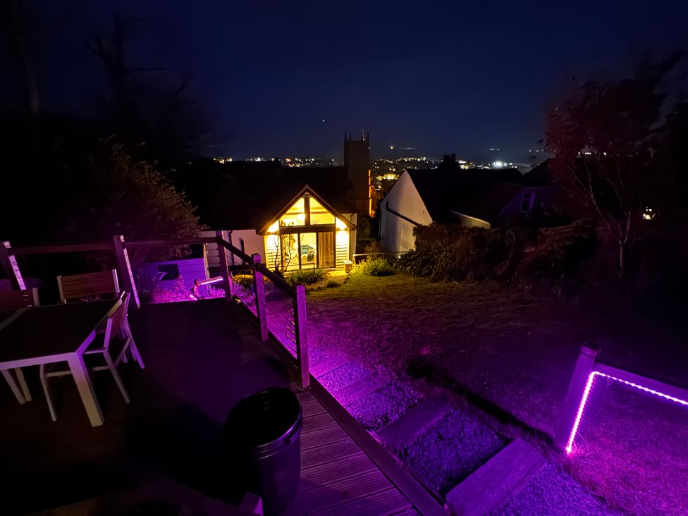 A backyard with a deck and table chairs illuminated in purple lighting at Overchurch in Hythe