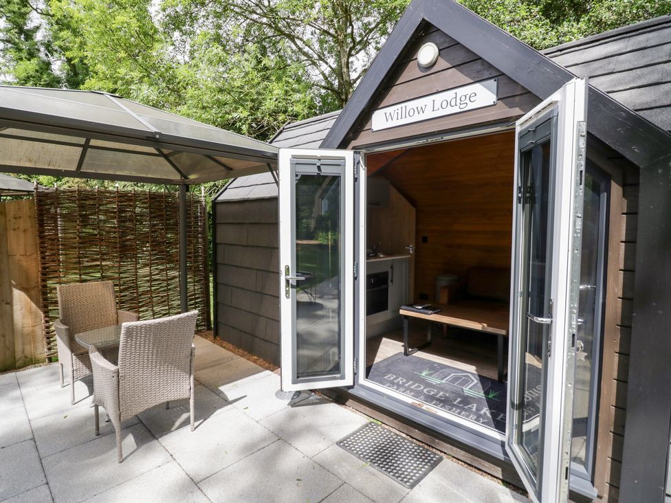 A cabin with an open door and outdoor seating area at Willow Lodge At Bridge Lake Farm & Fishery Chacombe