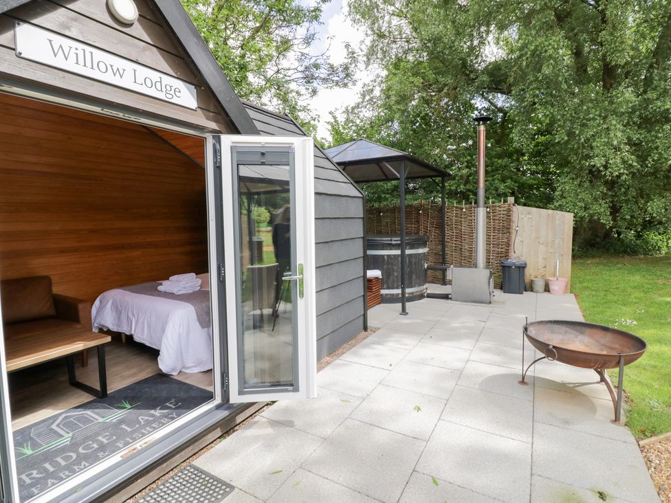 An outdoor area with a lodge, hot tub, and seating at Willow Lodge At Bridge Lake Farm & Fishery Chacombe