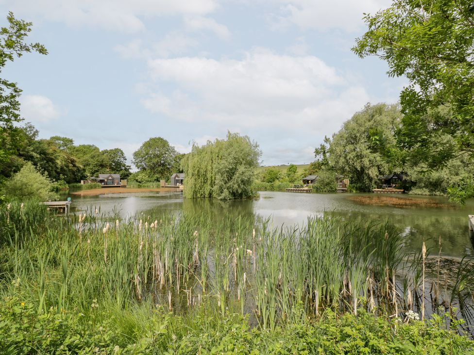 A lake surrounded by greenery and cottages at Willow Lodge At Bridge Lake Farm & Fishery, Chacombe