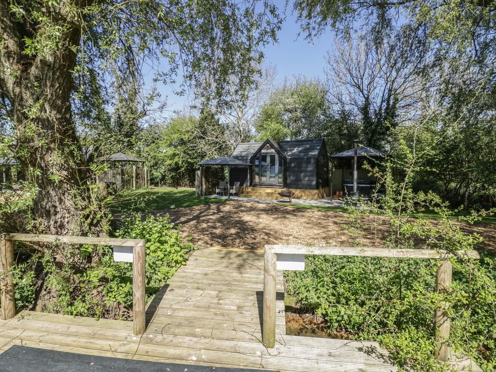A garden with a cabin and wooden deck at Willow Lodge At Bridge Lake Farm & Fishery Chacombe