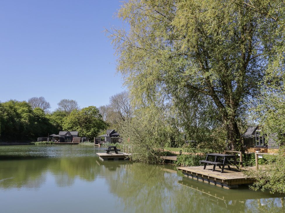 A lake with dock and seating area at Willow Lodge At Bridge Lake Farm & Fishery Chacombe