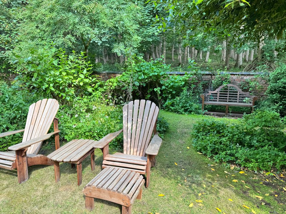 A garden with wooden chairs and a bench at Sunny Cottage in Grantham