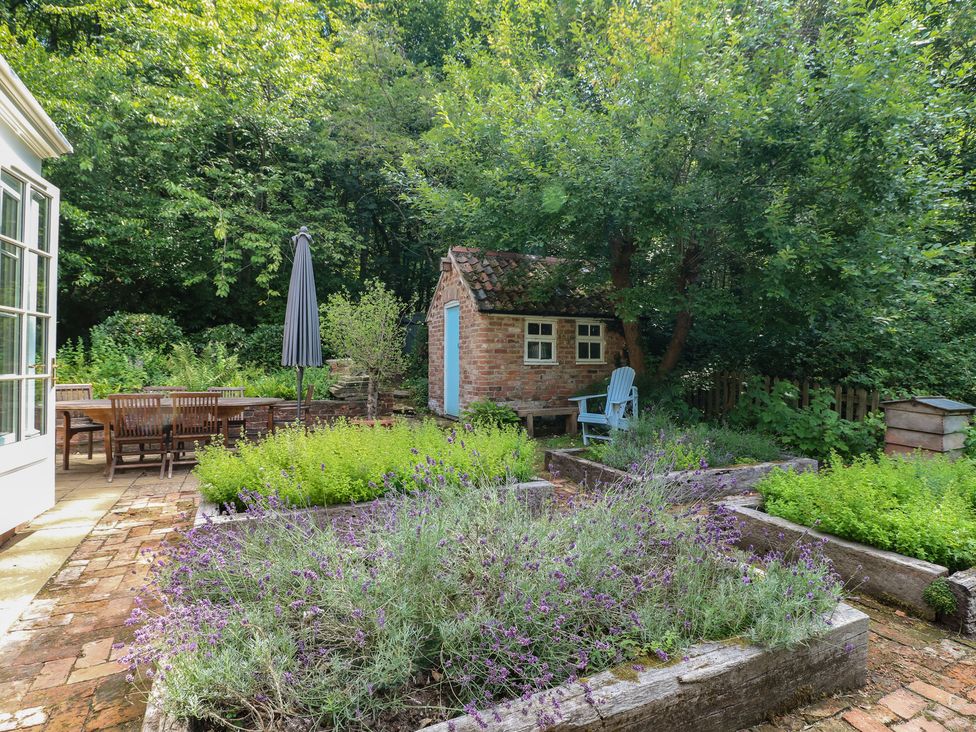 A garden with a table, chairs, a shed, and flower beds at Sunny Cottage in Grantham