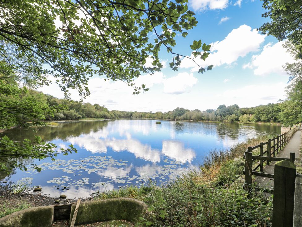 A lake surrounded by trees and a fenced path at Corner House Cottage in Mapperley Village