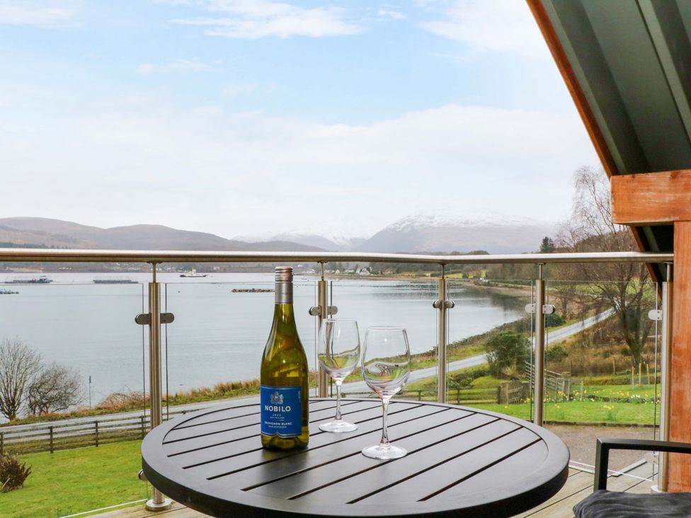 An outdoor balcony with a bottle of wine and glasses overlooking a water view at The Apartment in Ardgour
