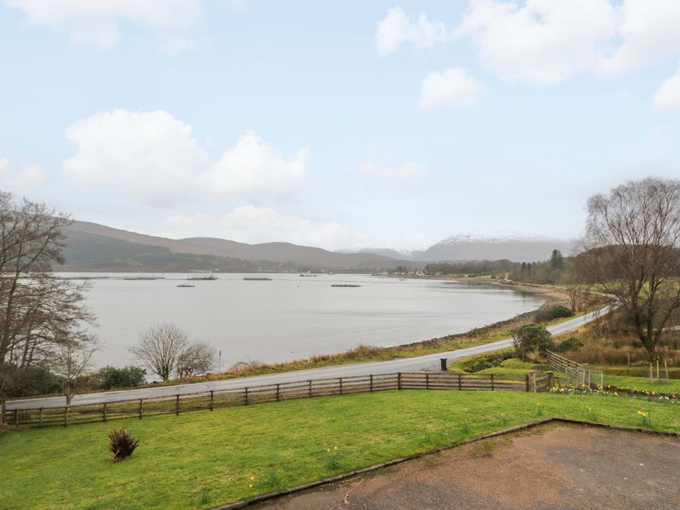 A lake with a road and mountains in the background at The Apartment in Ardgour