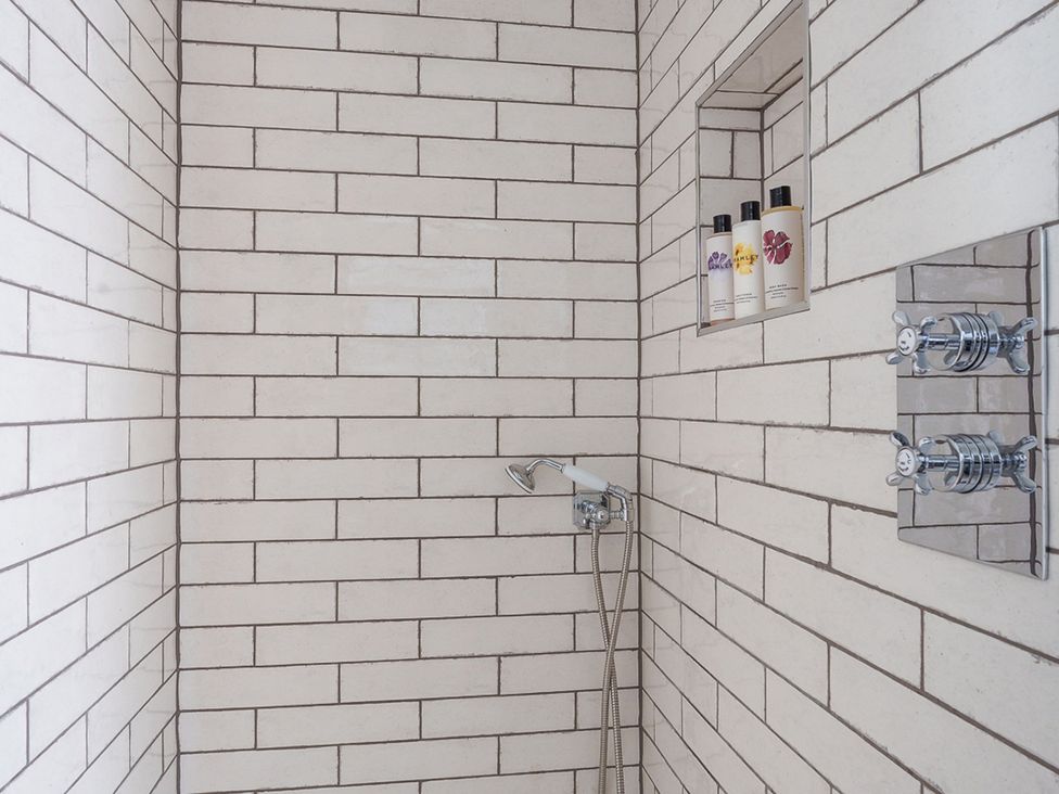A shower area with tiling and body wash bottles at Reybridge House in Lacock