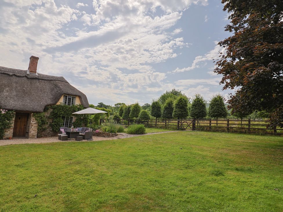 A thatched roof house with outdoor seating and trees at Garden View in Wellington
