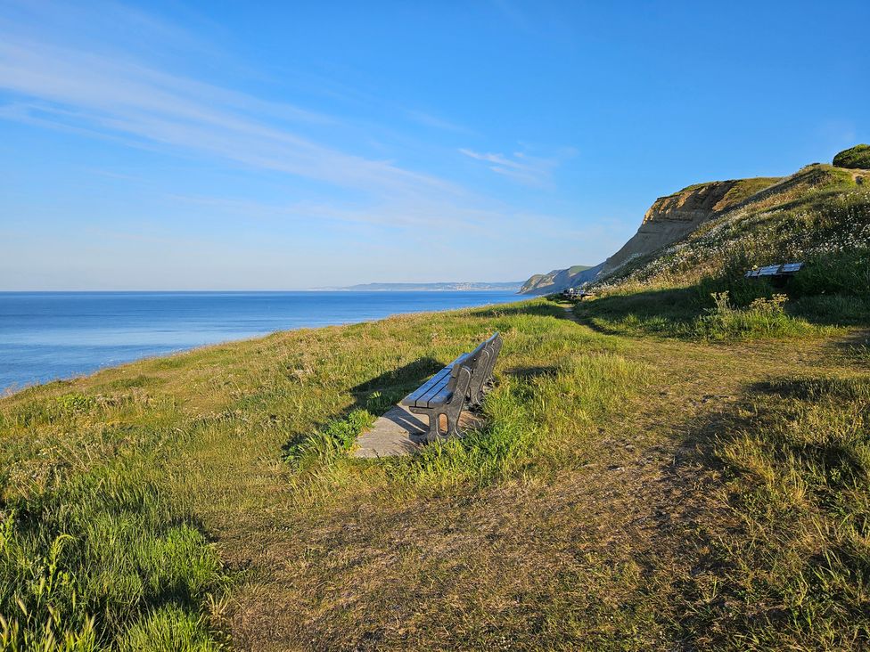 A coastal cliff area with benches facing the sea and a clear sky at Sandy Combe in West Bay