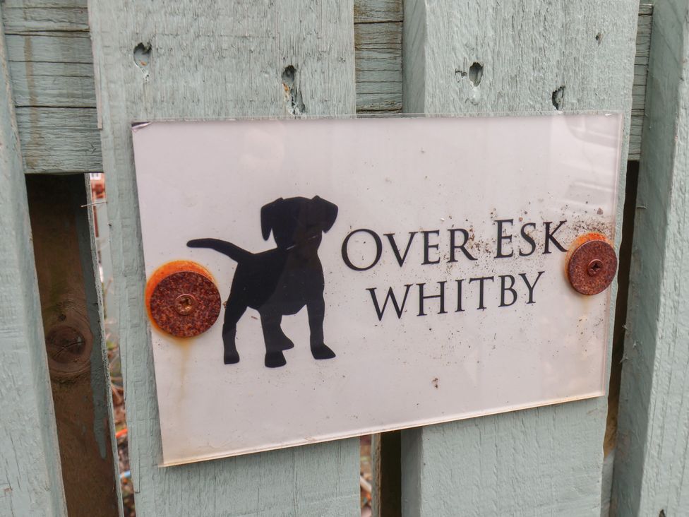 A sign with a silhouette of a dog and the text Over Esk Whitby mounted on a wooden fence