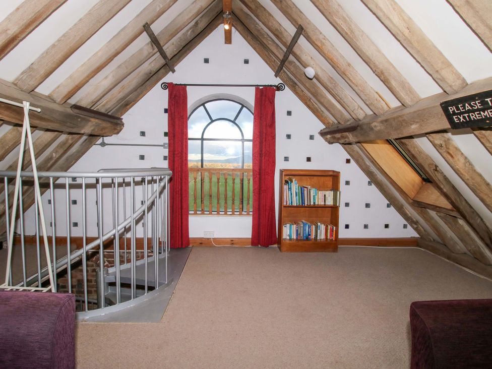 An attic with a window, bookshelf, and staircase at Windy Mundy Farm in Pitchford near Shrewsbury