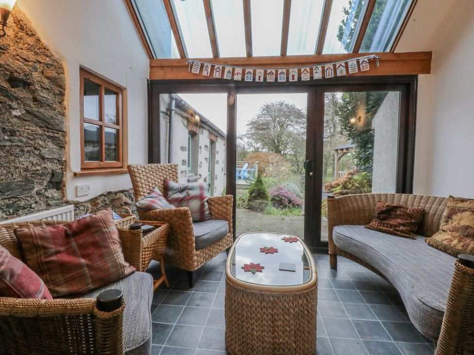 A conservatory with wicker furniture and large windows at Ty Gwennol Llanfaethlu