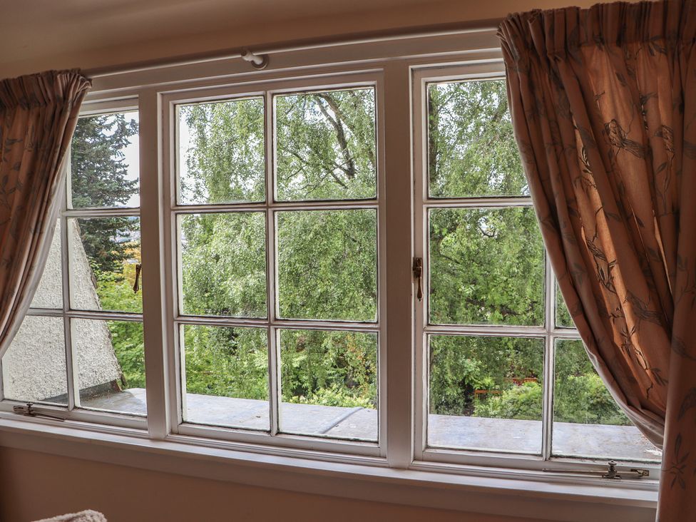 A window with curtains overlooking trees at Branklyn Garden Cottage Perth