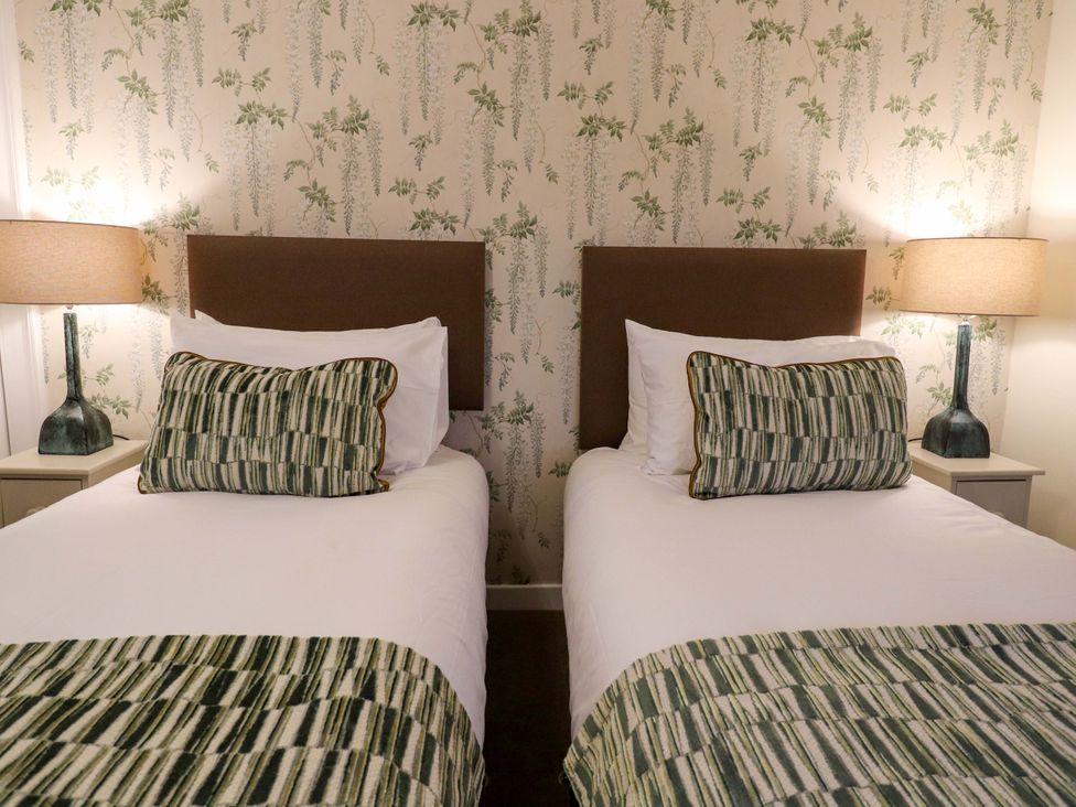 A bedroom with two beds, nightstand, and lamps at Paye House - Cromarty