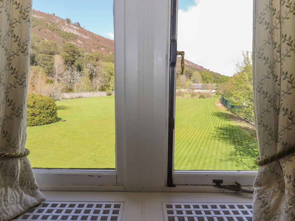 A view of a lawn and trees from a window at Bynack - Mar Lodge Estate in Braemar