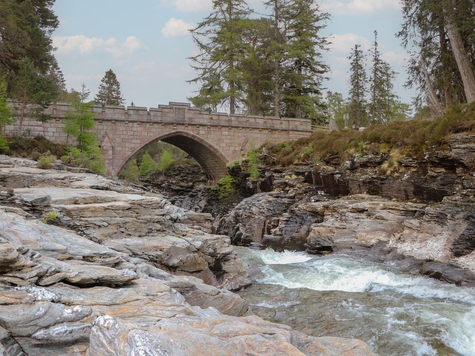 A bridge over a river with rocks and trees at Macdui - Mar Lodge Estate Braemar