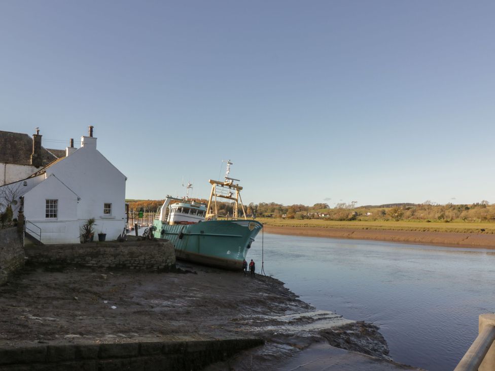 A boat docked by the river with a house nearby at Blue Door - Kirkcudbright in Kirkcudbright