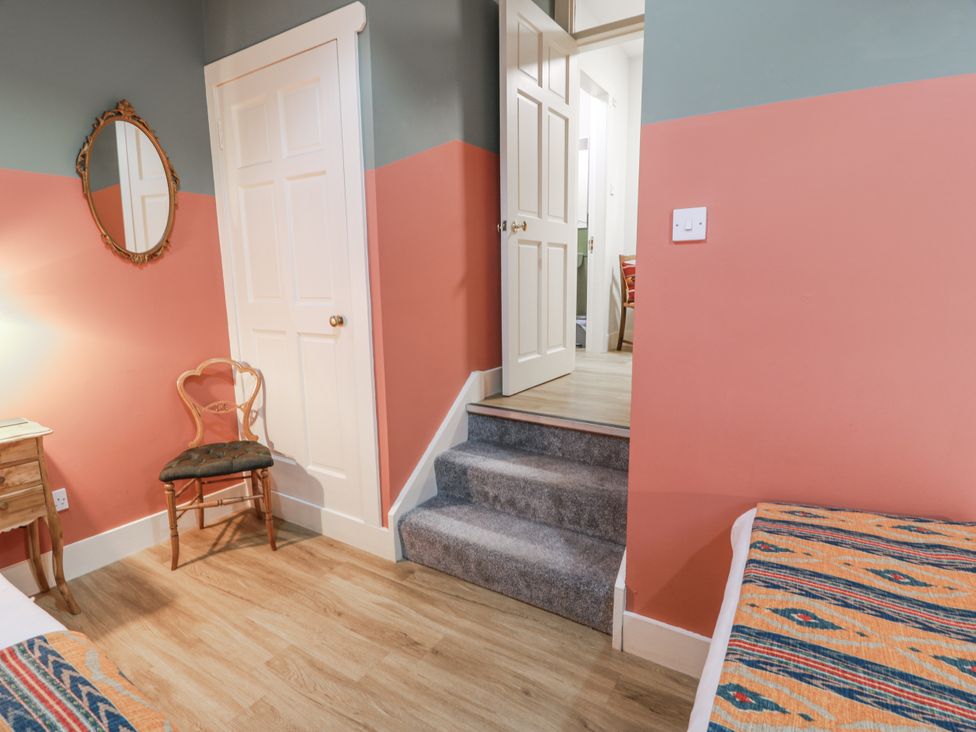 A bedroom with a bed, chair, and staircase leading to another room at The Coach House - Holmwood, Glasgow