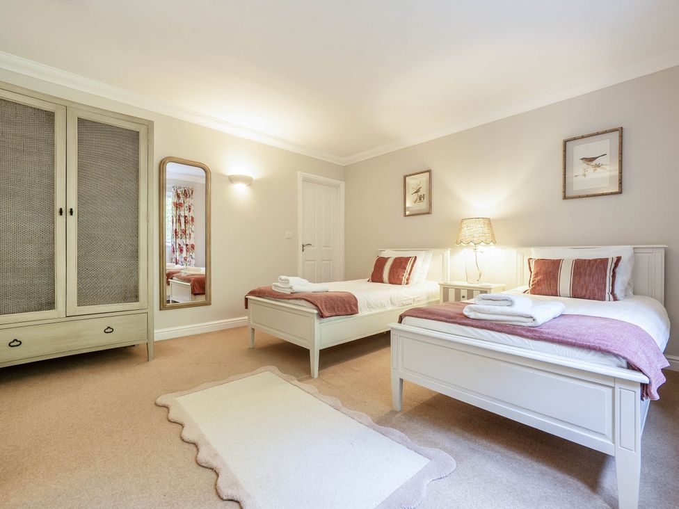 A bedroom with two beds and a wardrobe at Cunsey Lodge at the Graythwaite Estate