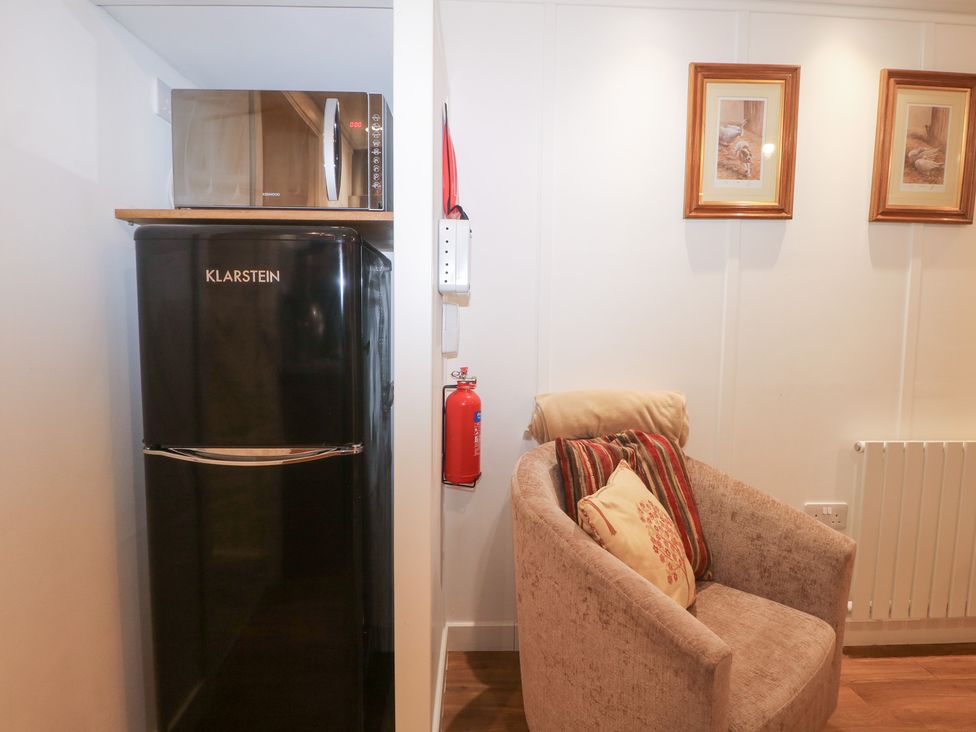 A fridge, microwave, armchair, and fire extinguisher at Orchard Lodge in Bolney